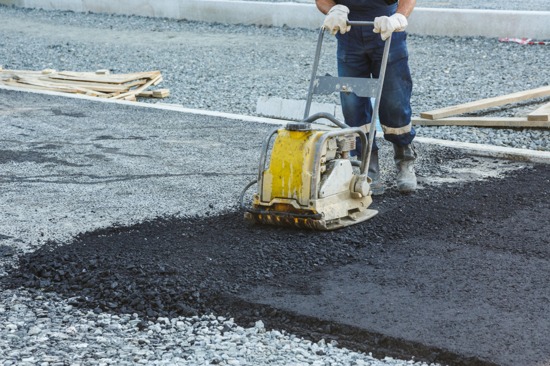 Plate compactor tamping new asphalt over a freshly prepared stone base