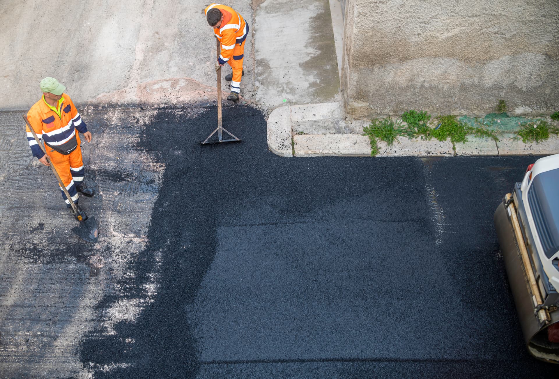 Two-man crew hand-raking a newly paved residential driveway