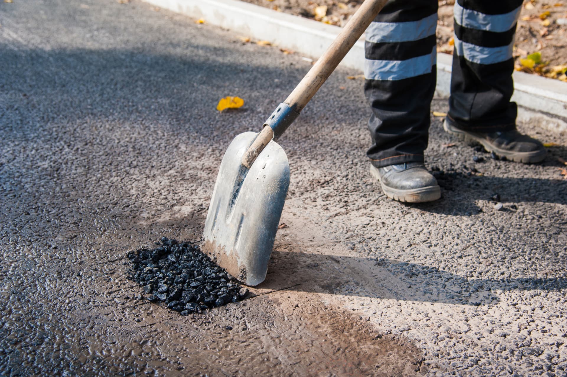 Worker finishing the edge of a freshly treated asphalt surface with a shovel