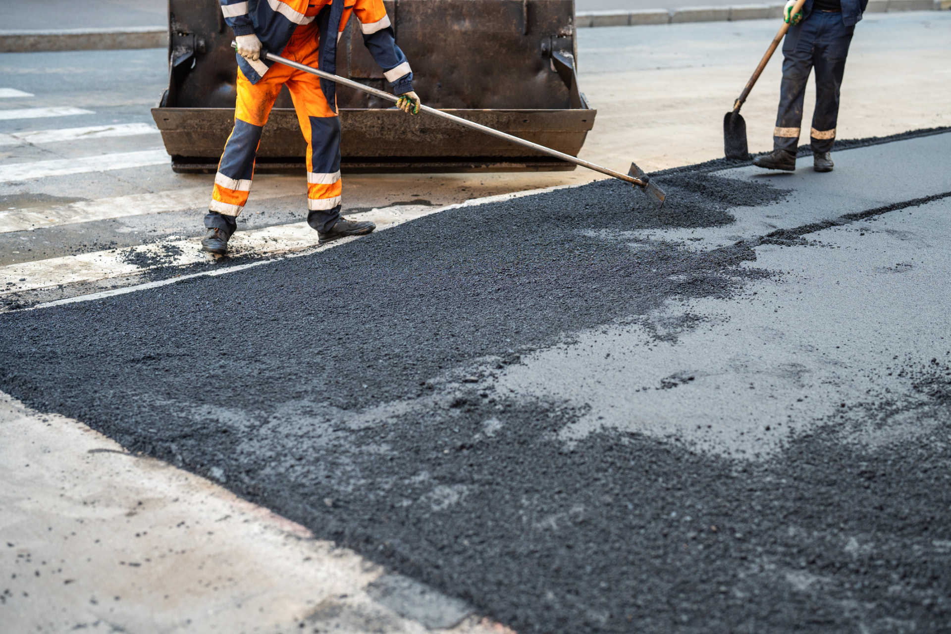 Crew smoothing a freshly treated asphalt surface across a street