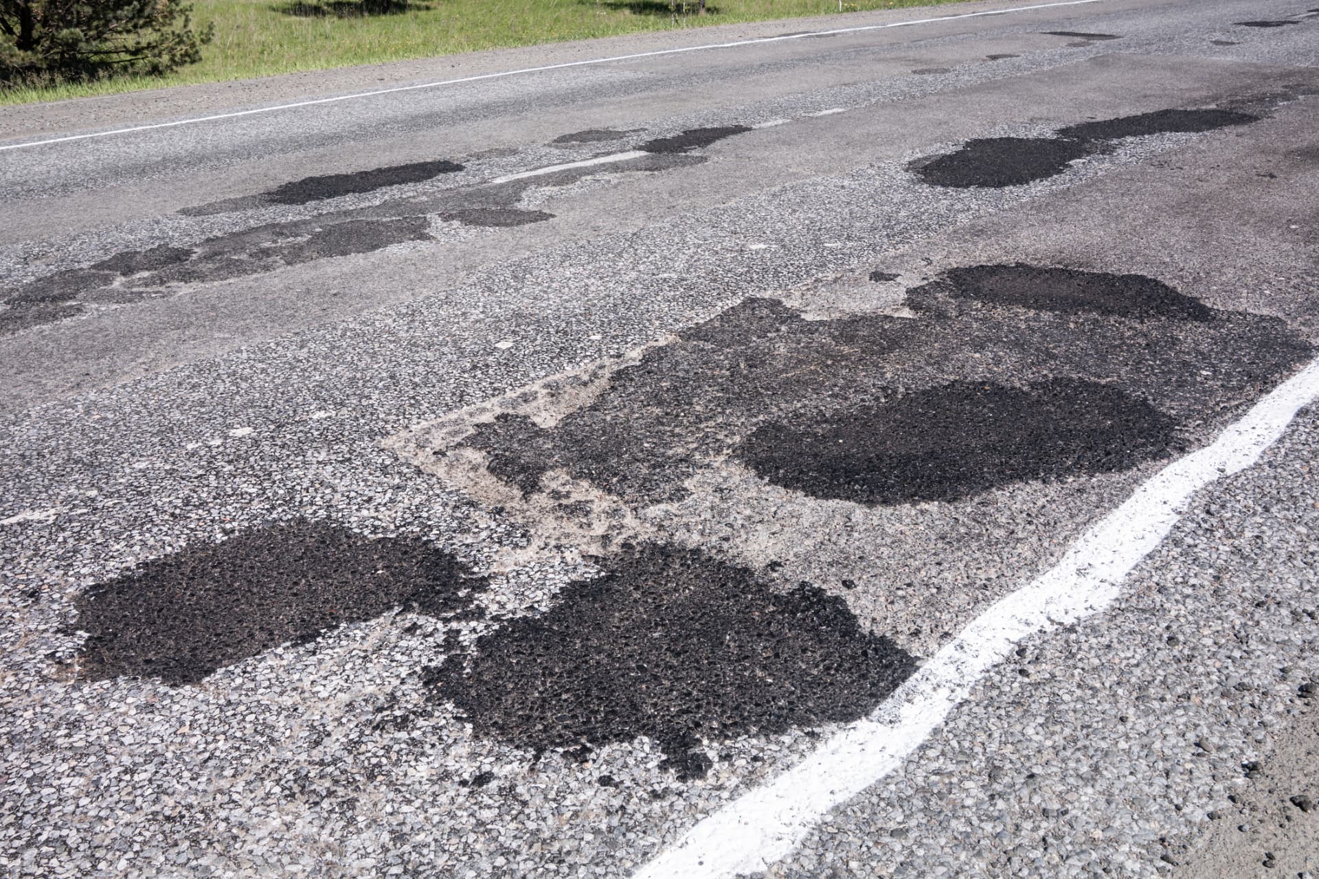 Roadway showing multiple completed asphalt patch repairs along the travel lane