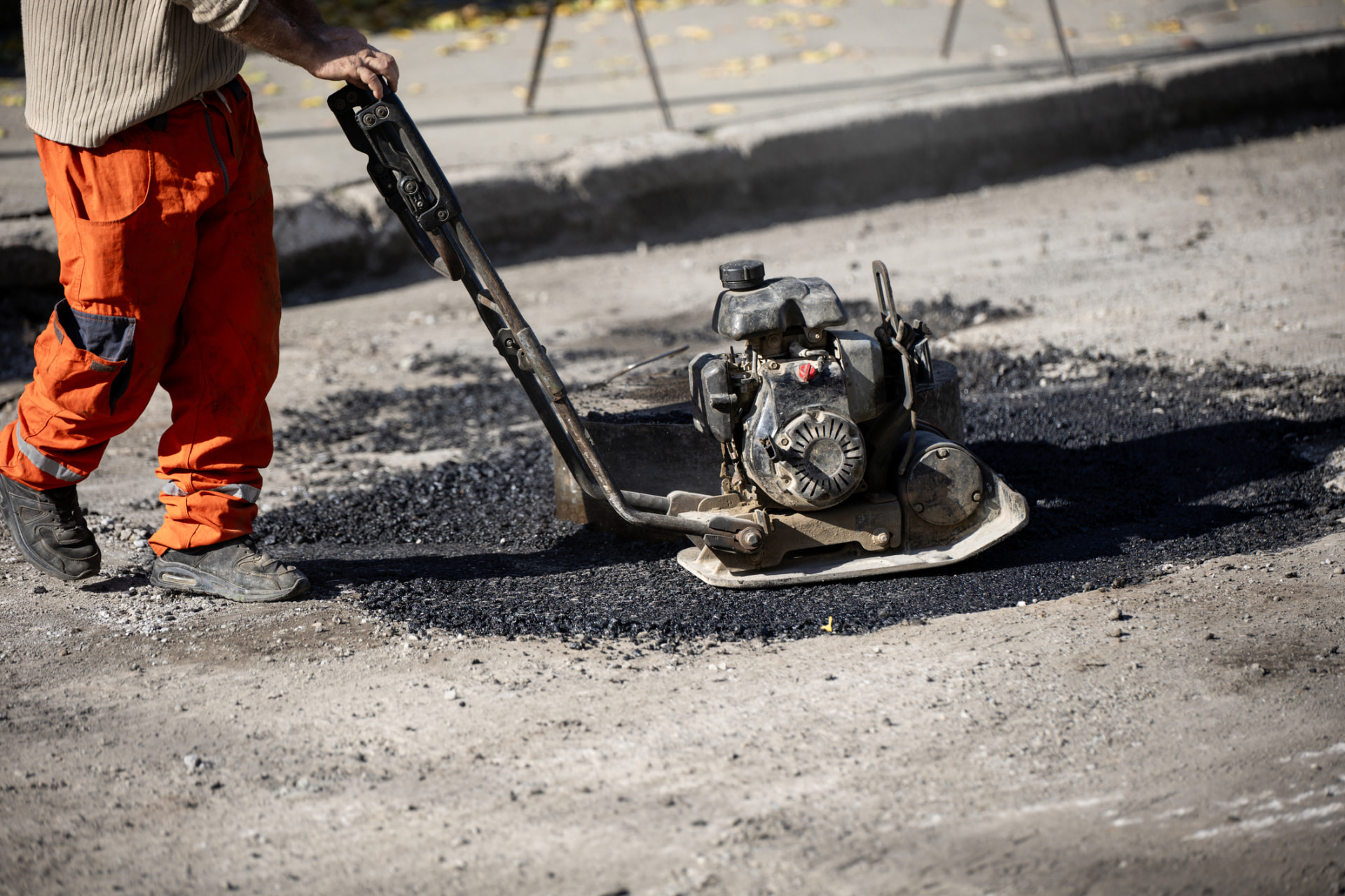 Worker running a plate compactor over a fresh asphalt repair in Middletown, NJ