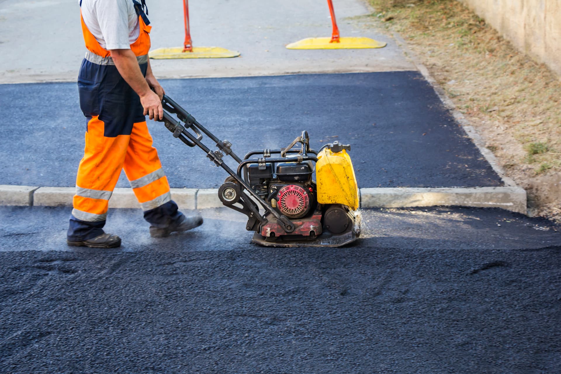 Worker compacting a fresh asphalt patch with a plate compactor