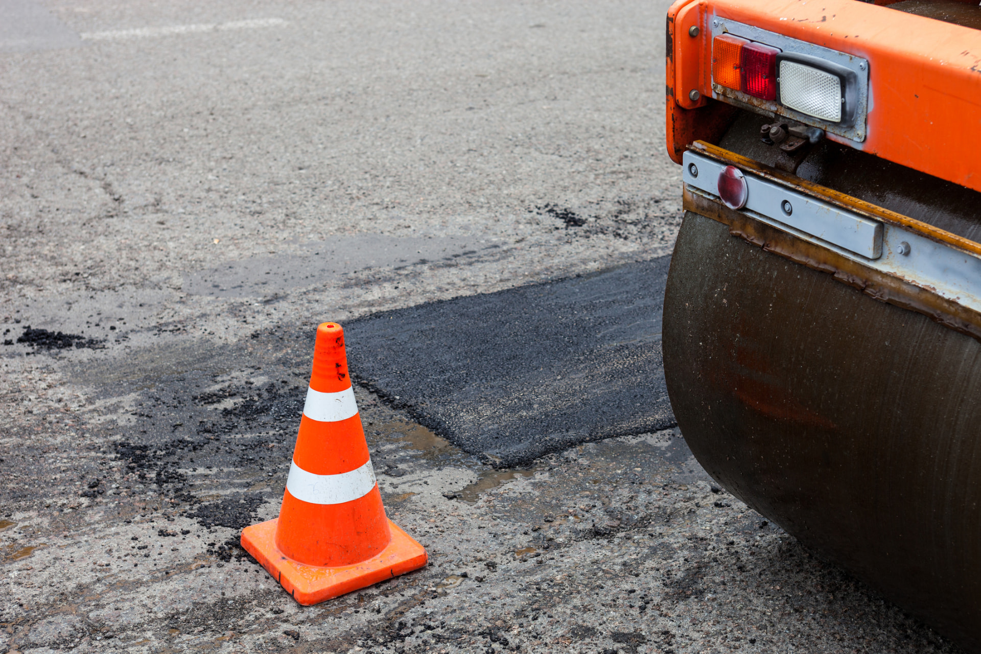Asphalt roller and safety cone beside a freshly repaired section of pavement