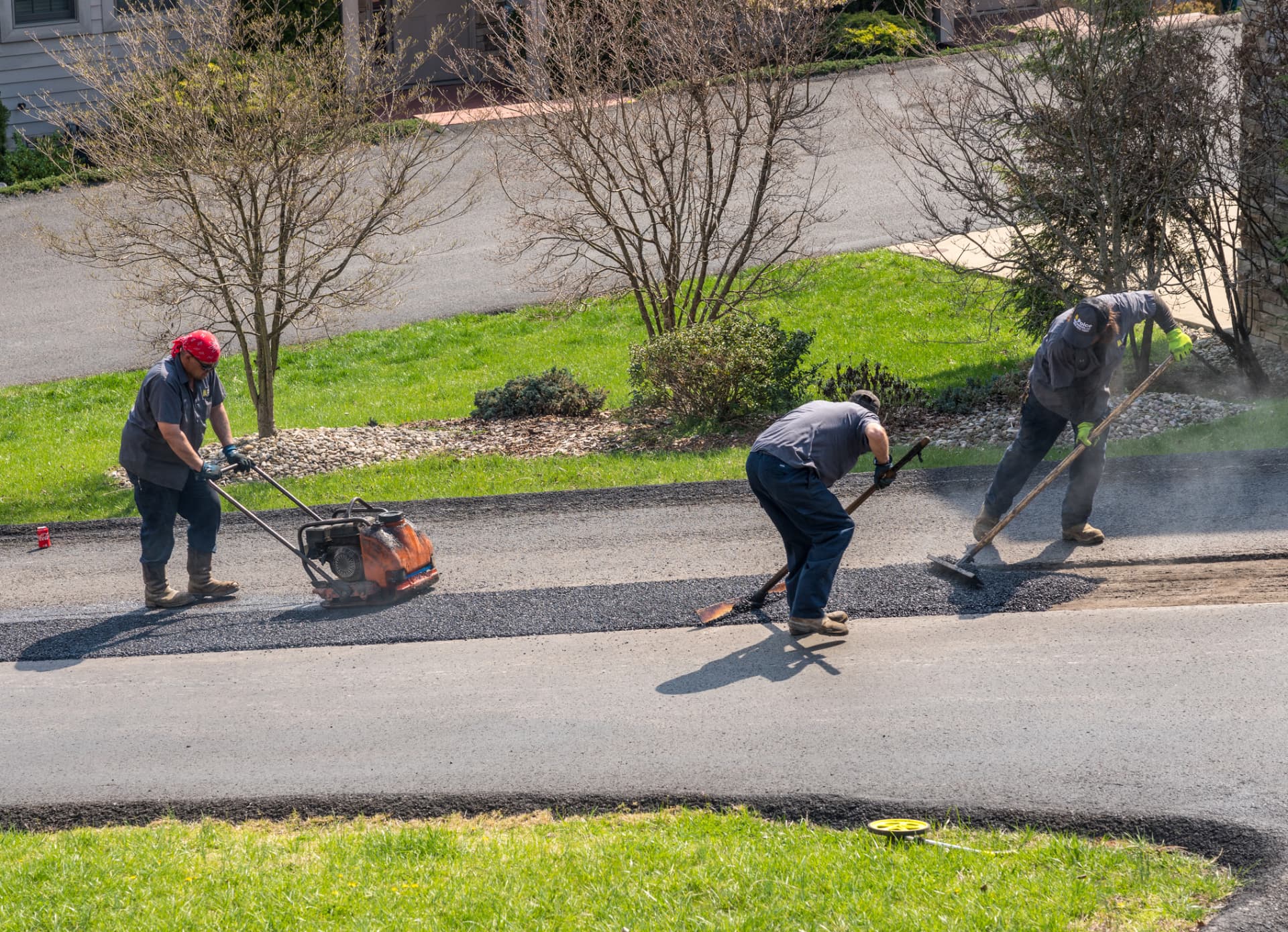 Crew compacting and raking a new asphalt driveway apron at a Toms River home
