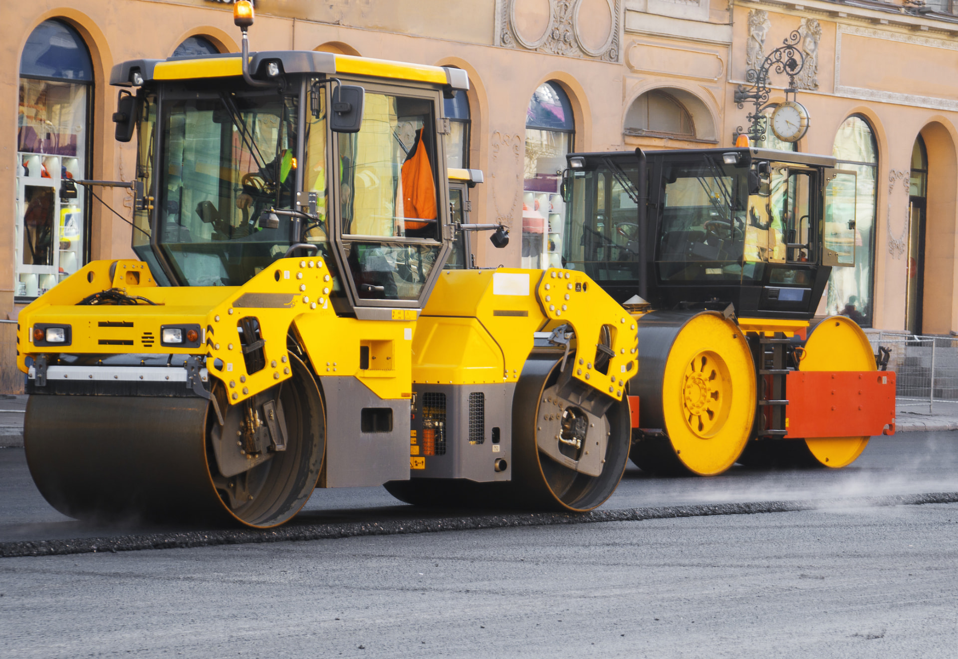 Two tandem rollers compacting a freshly paved street through a business district