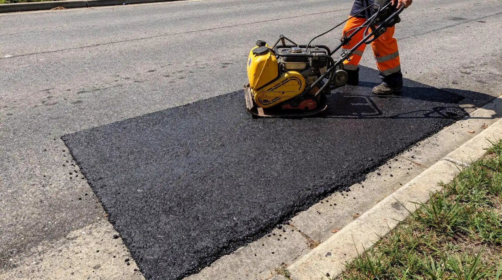 Plate compactor pressing a fresh hot-mix asphalt patch flush with the road