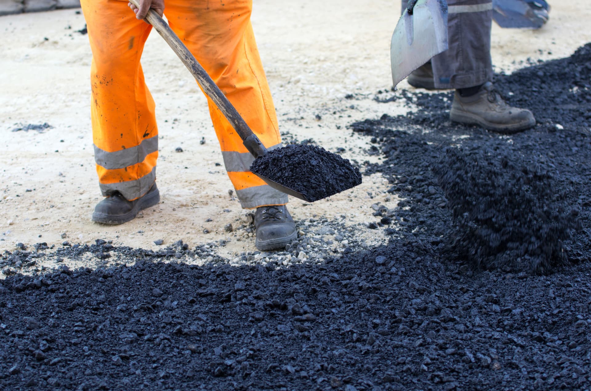 Crew shoveling hot-mix asphalt over a prepared stone base for a new driveway