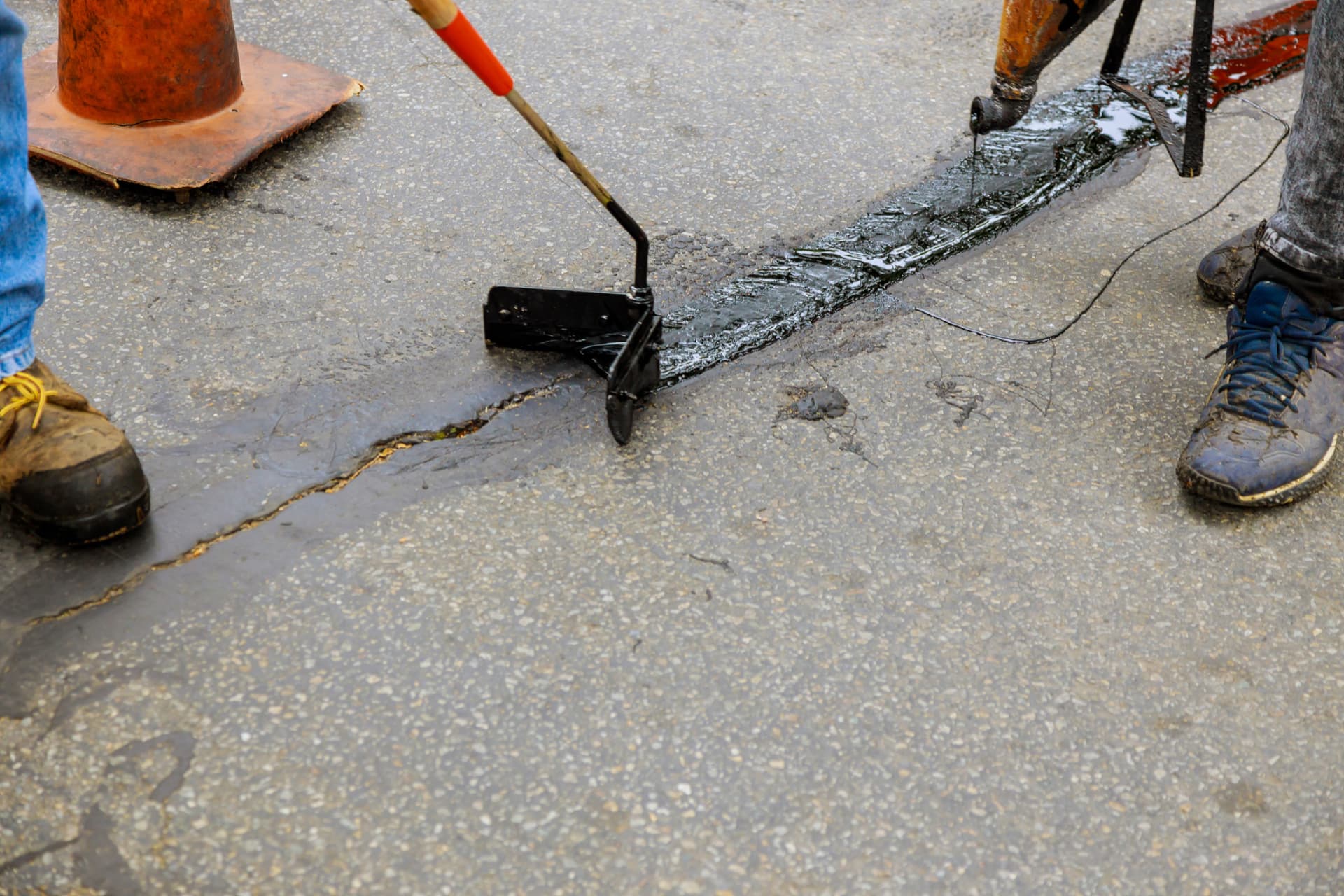 Worker squeegeeing hot crack sealant along a pavement joint