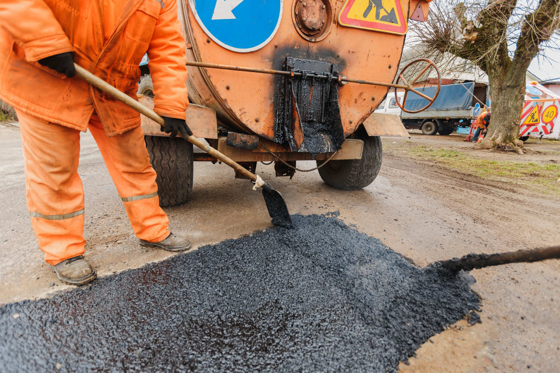 Worker spreading hot asphalt mix from a tar kettle to repair a damaged road section