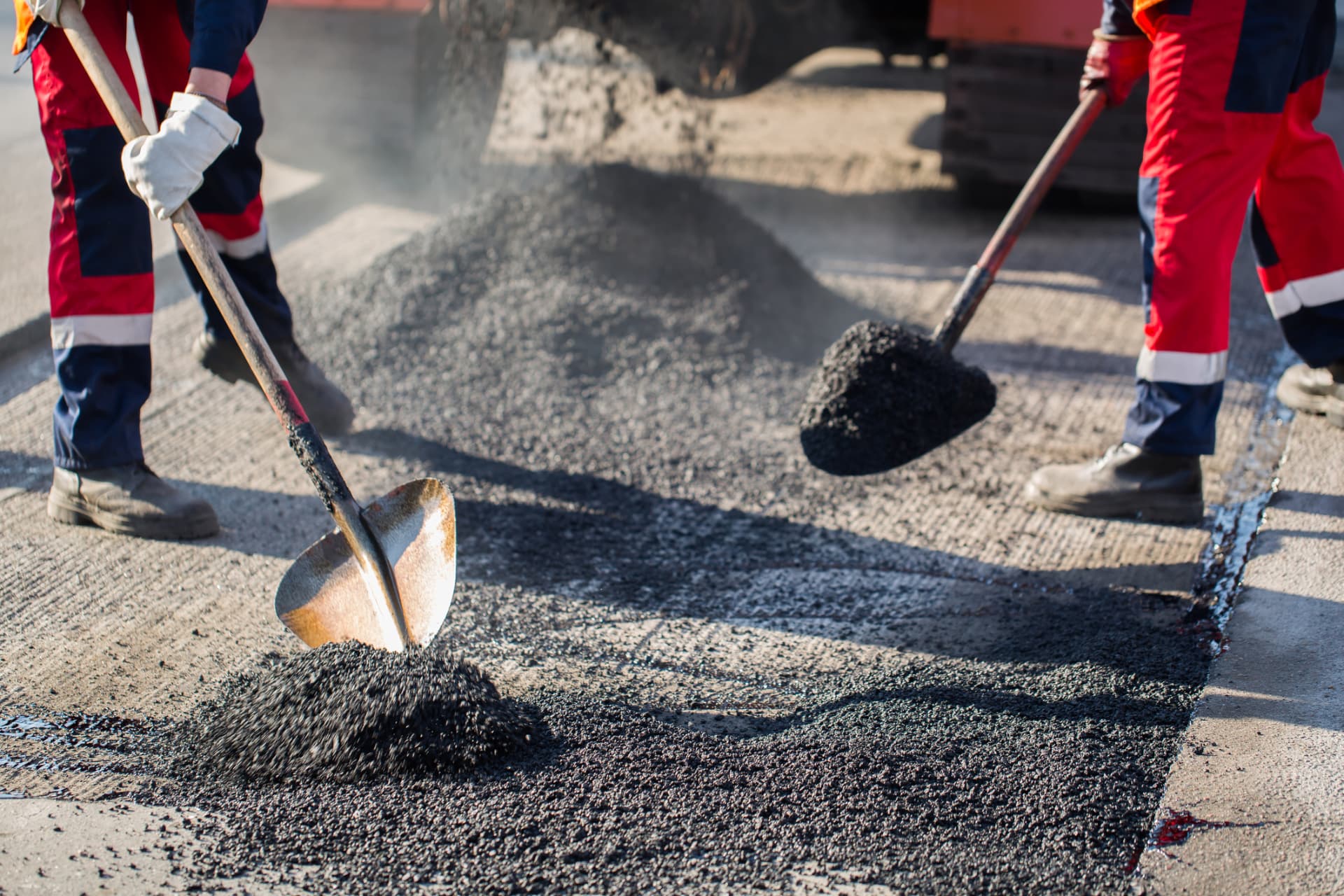 Two paving workers shoveling hot-mix asphalt on a repair in Edison, NJ