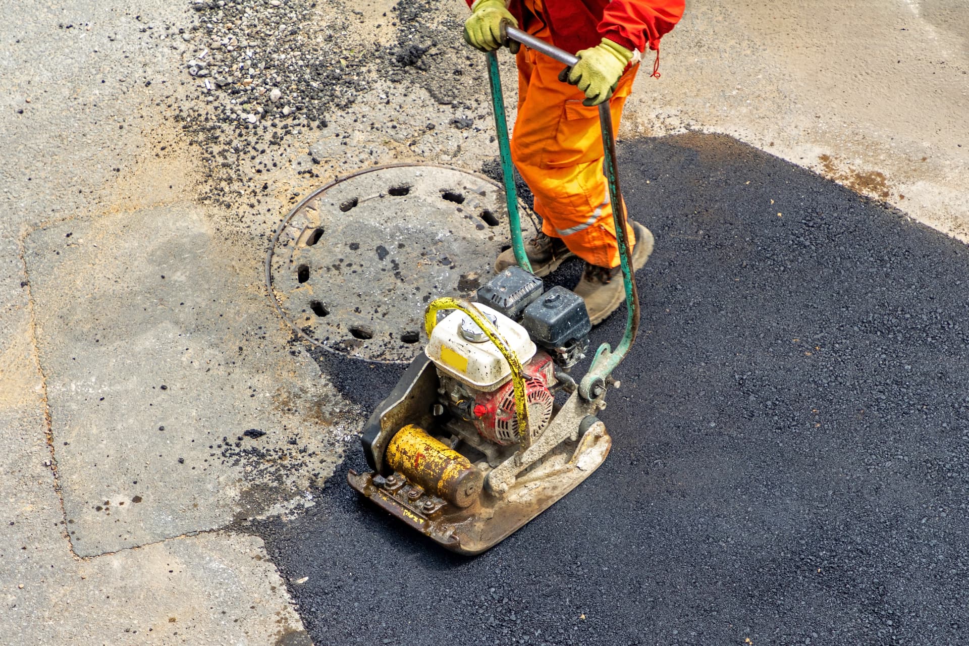 Worker compacting an asphalt repair with a plate compactor