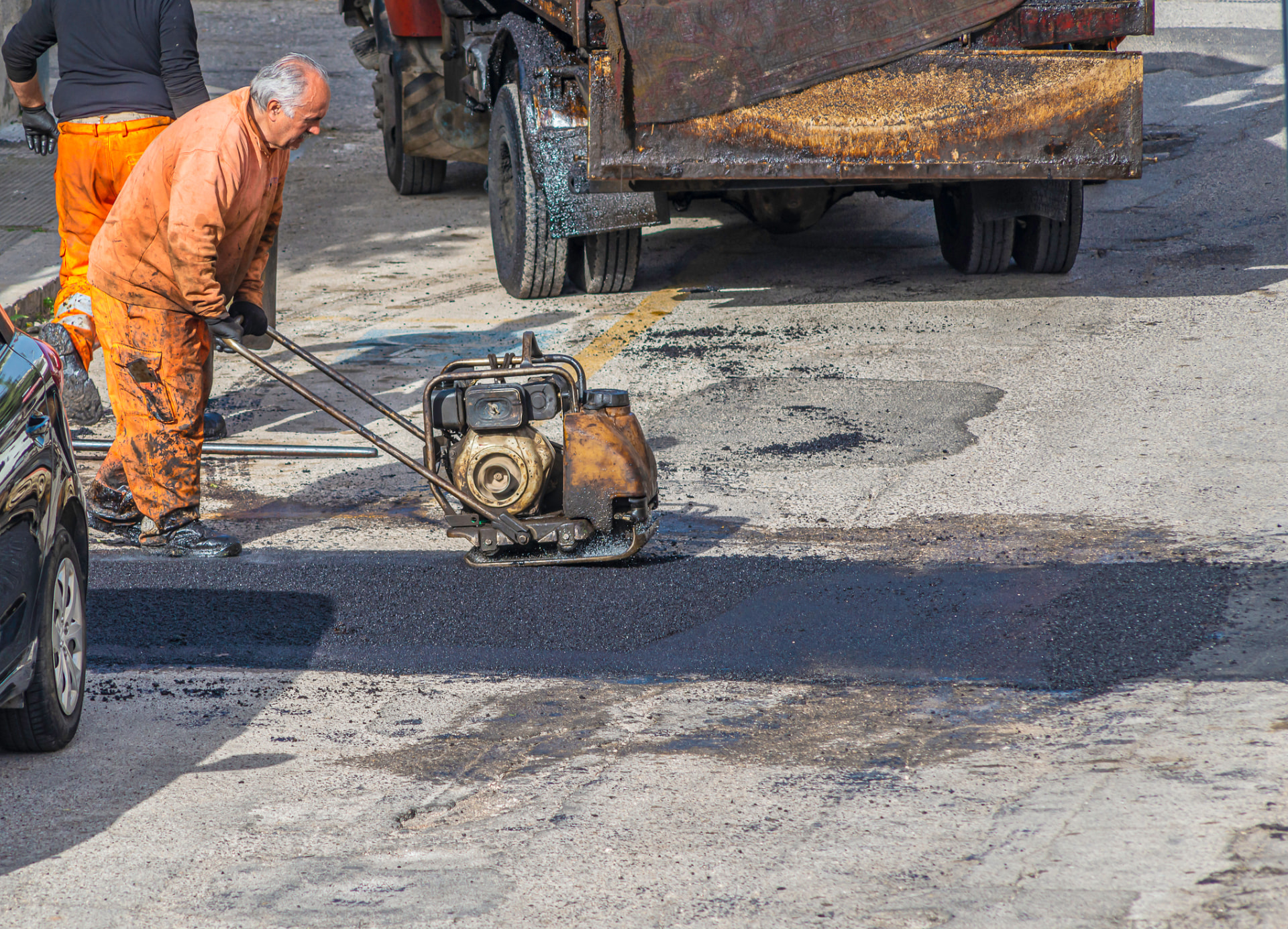 Crew compacting a hot-mix asphalt pothole repair in a roadway
