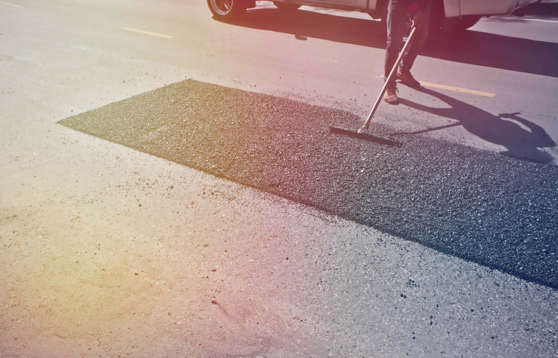 Worker raking a fresh asphalt patch into a repaired road section