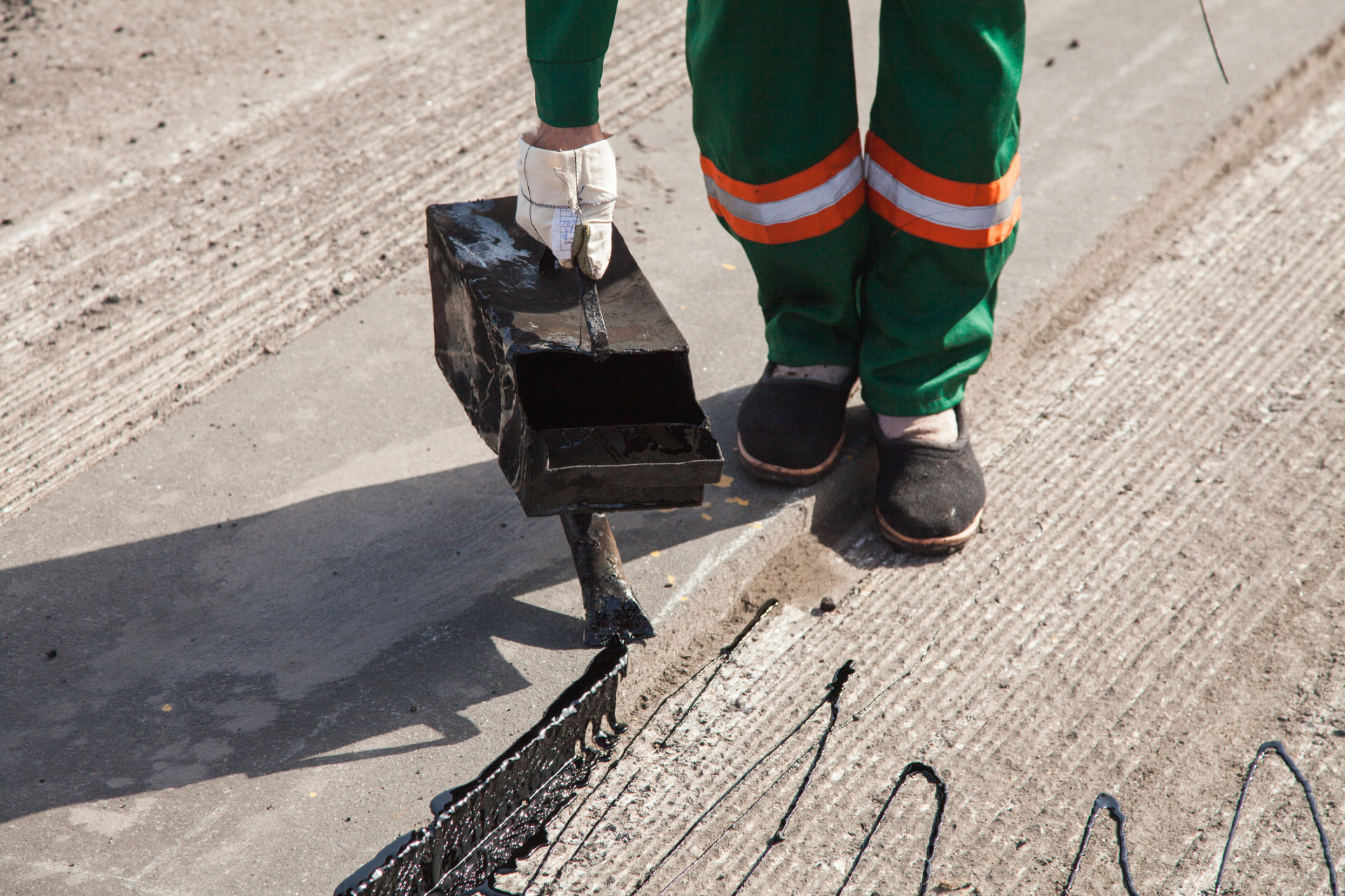 Worker pouring hot sealant from a pour pot into a pavement joint