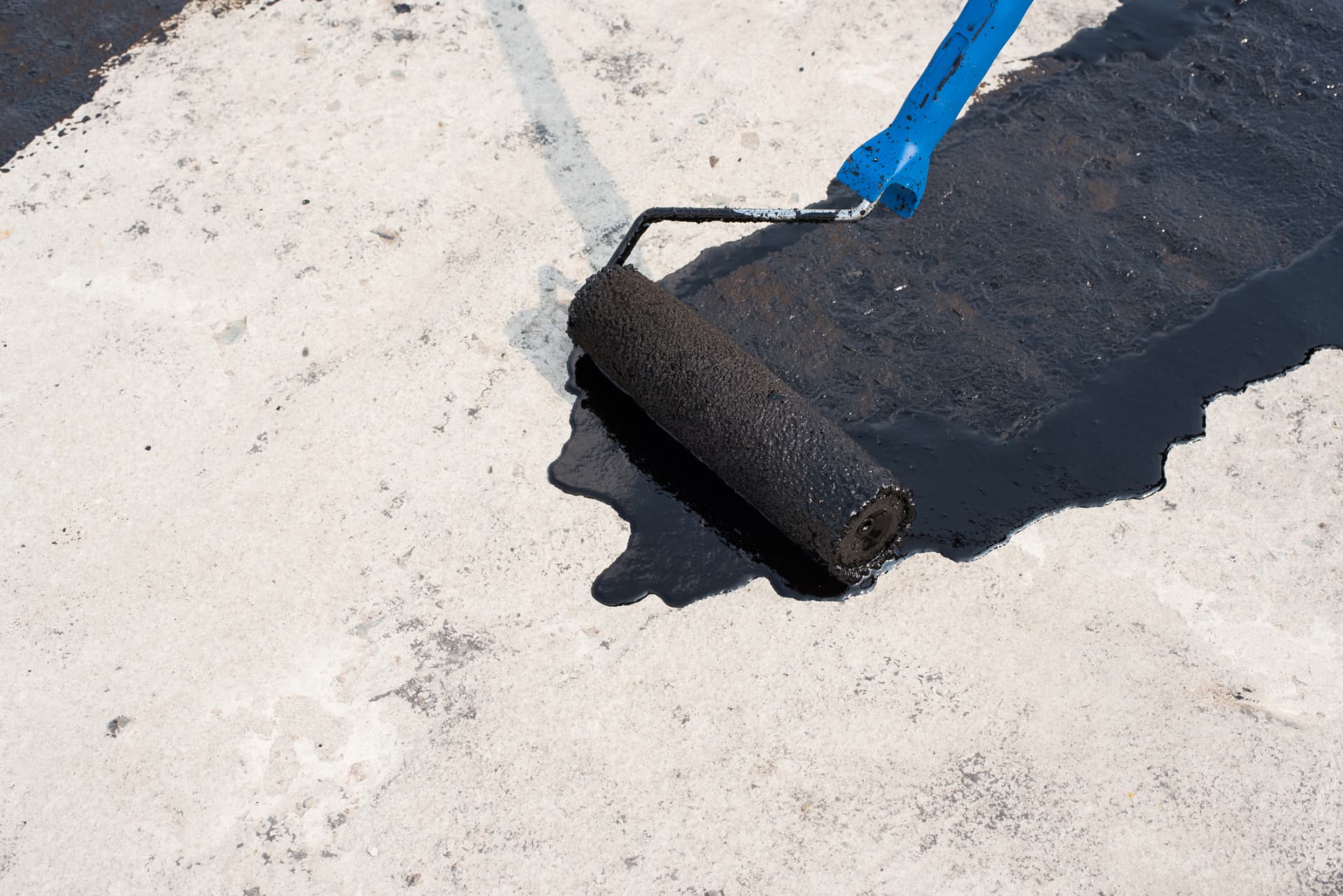 Roller applying black sealer over a light-colored pavement surface in Middletown