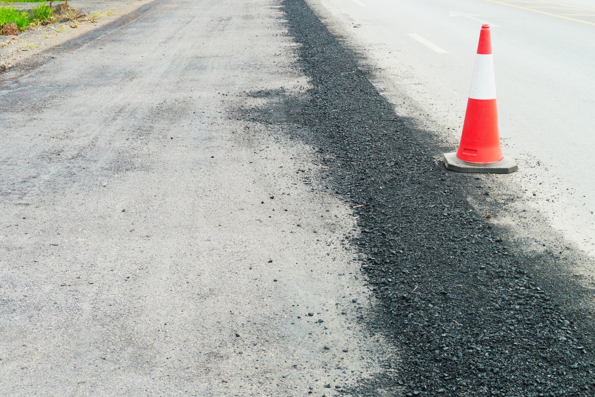 New asphalt shoulder built along the edge of an existing roadway beside a traffic cone