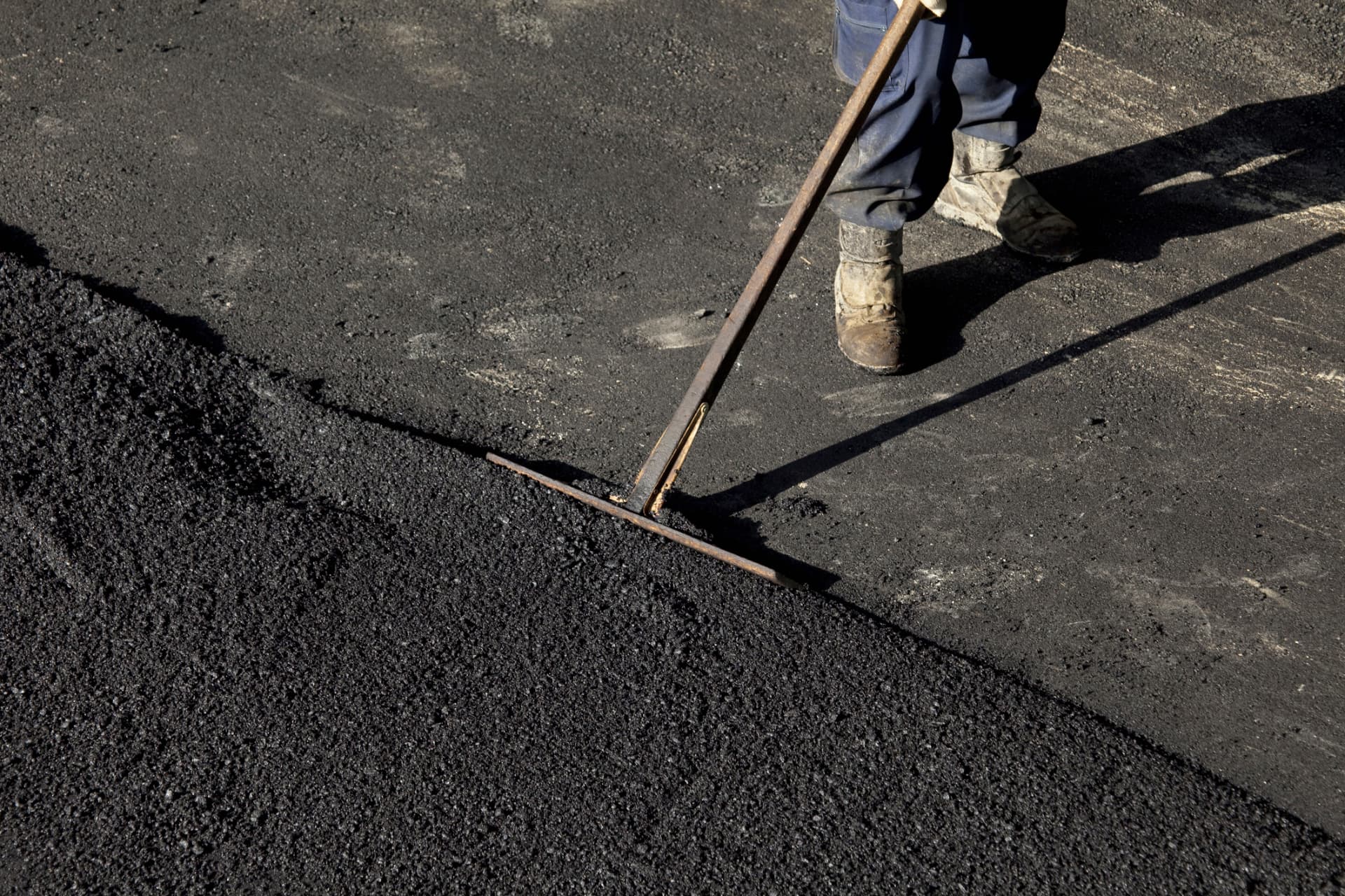 Paving crew member raking the edge of new hot-mix asphalt in Toms River, NJ