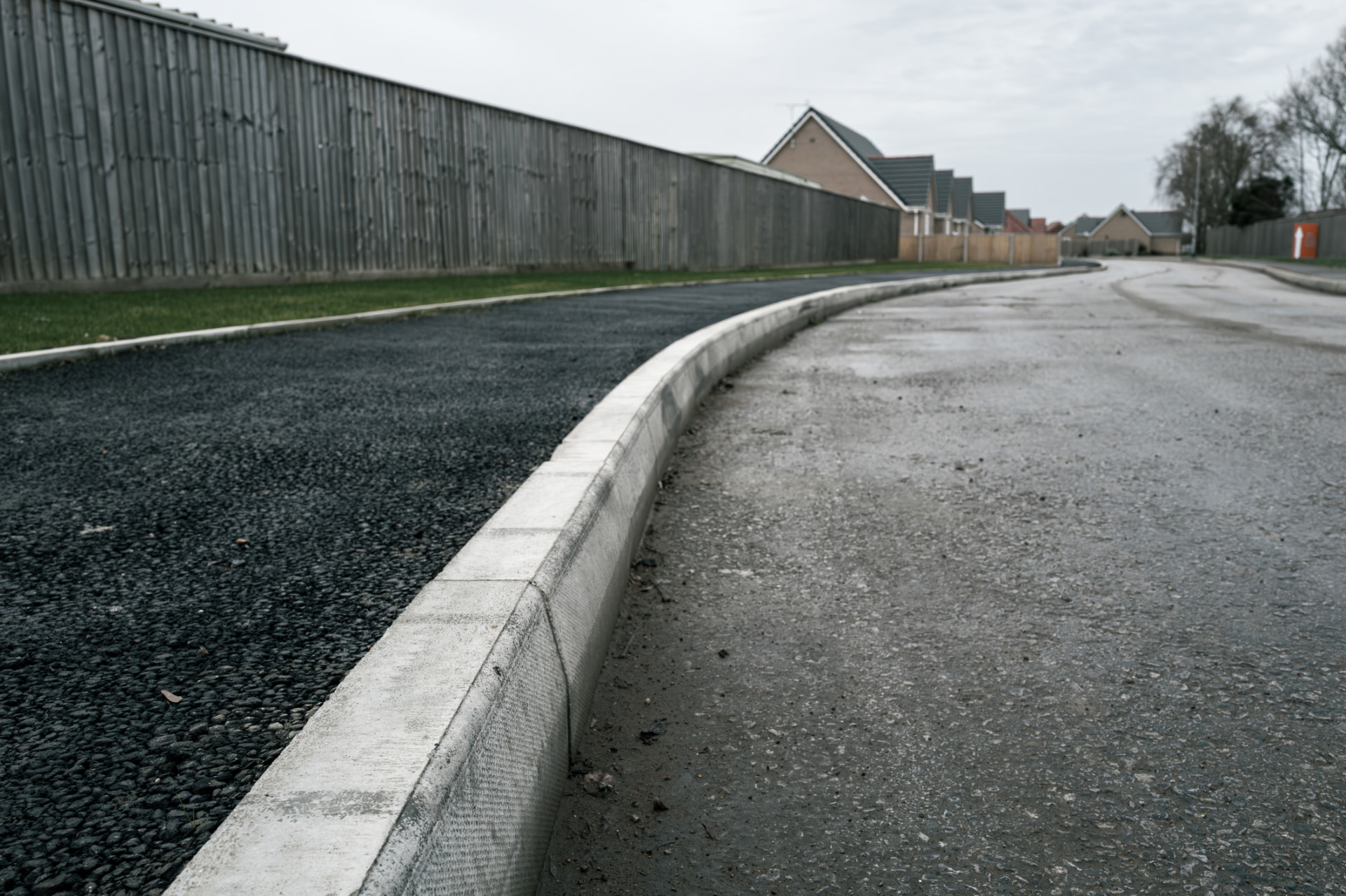 Freshly laid asphalt beside a concrete curb on a residential street