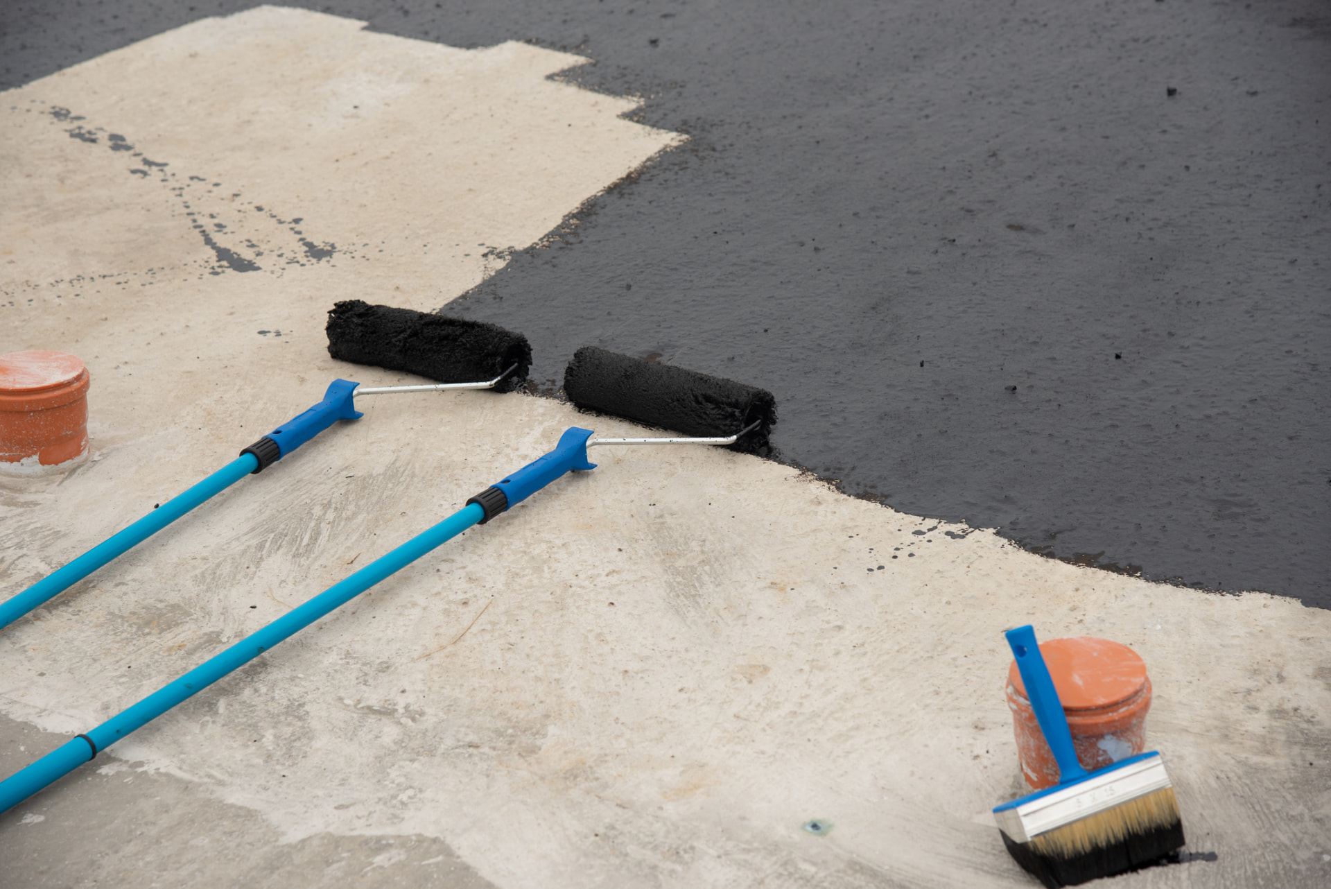 Sealcoating rollers and brush beside a half-sealed asphalt surface