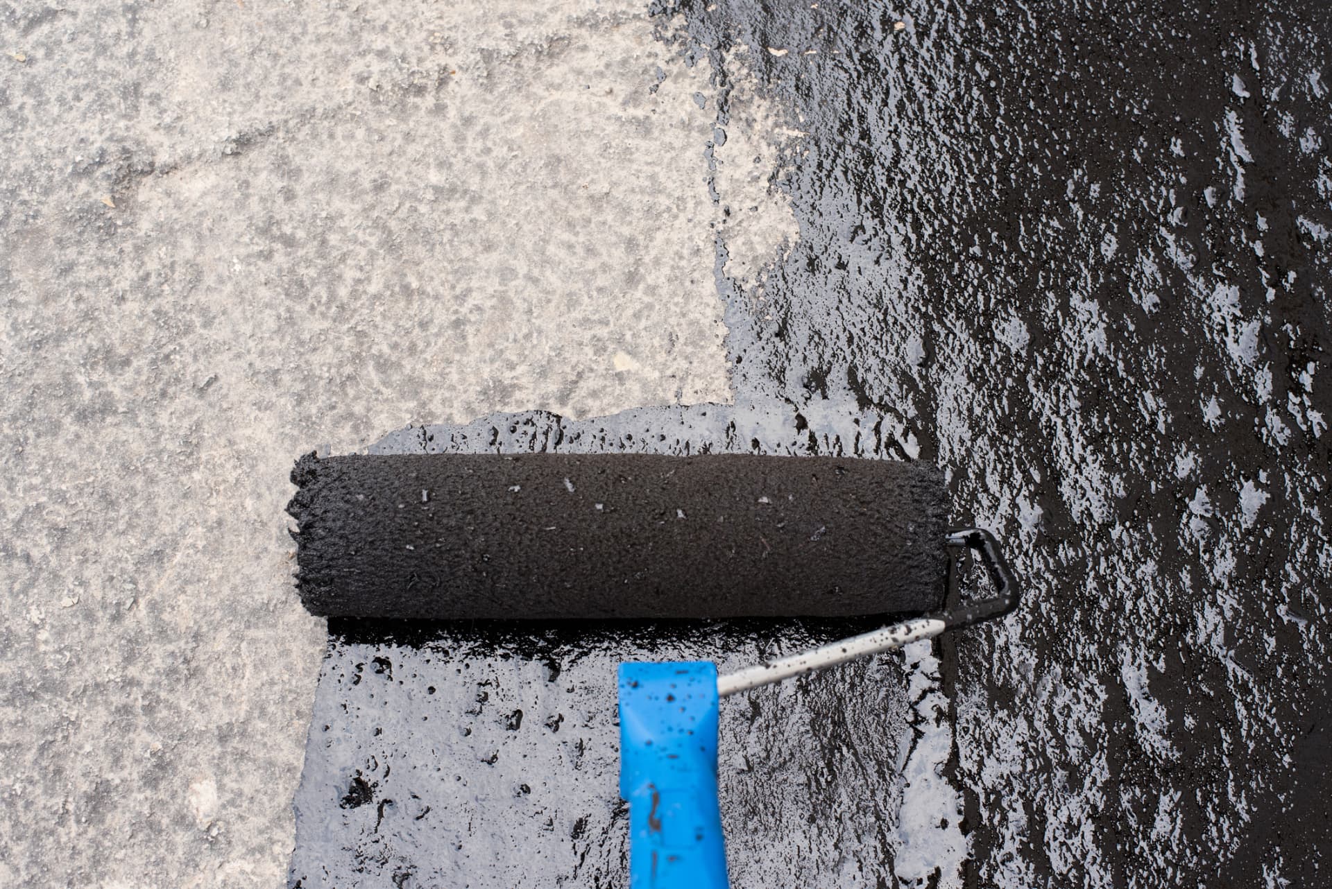 Roller applying fresh black sealer over weathered gray pavement