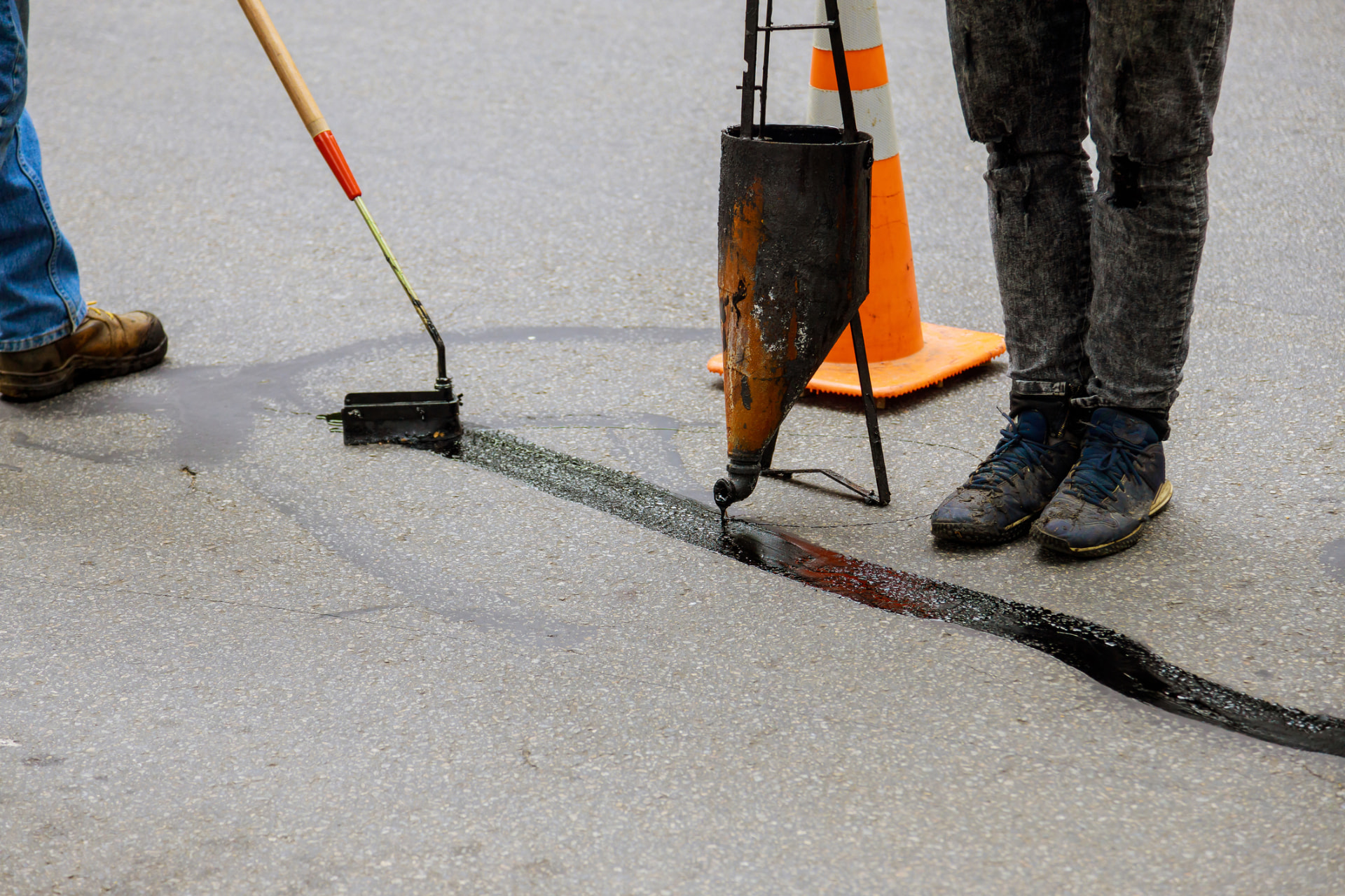 Crew sealing a long crack in an asphalt roadway with hot pour sealant and a squeegee