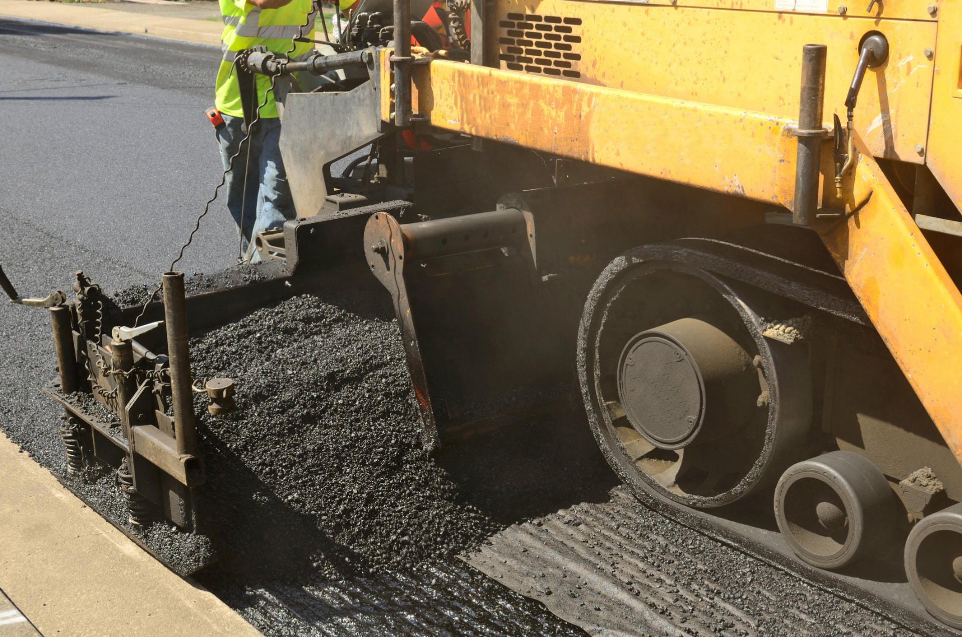 Paver screed spreading hot-mix asphalt along a concrete curb line